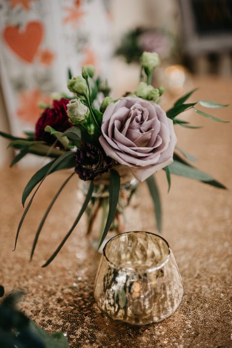 Rustic Boho Chic Wedding - Small arrangement made of a mauve rose, red rose and plum scabiosa on a gold sequin covered table.