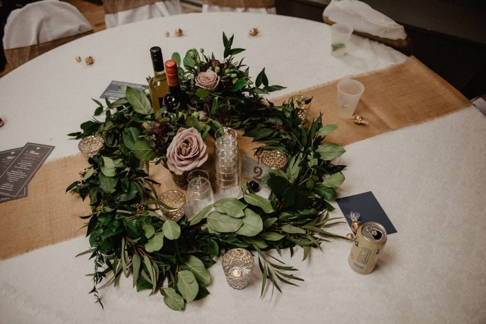 Rustic Boho Chic Wedding - Greenery wreath garland centrepiece made of salal, eucalyptus, italian ruscus, and mauve roses. The table is covered in ivory linens and a burlap table runner.