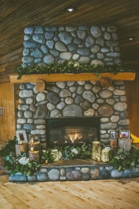 Cozy stone fireplace at the Cornerstone Theatre in Canmore, Alberta decorated with fresh greenery and white hydrangea garlands, candles, and photographs.