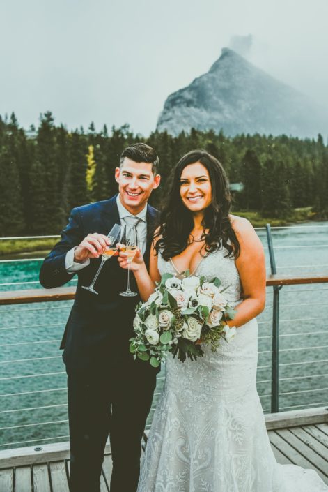 Meagan and Dwayne holding champagne and her bridal bouquet in the Rocky Mountains.