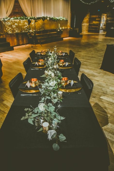 Black and Gold decorated table with a fresh garland made of white roses, eucalyptus and italian ruscus greenery complete with twinkly lights and candles.