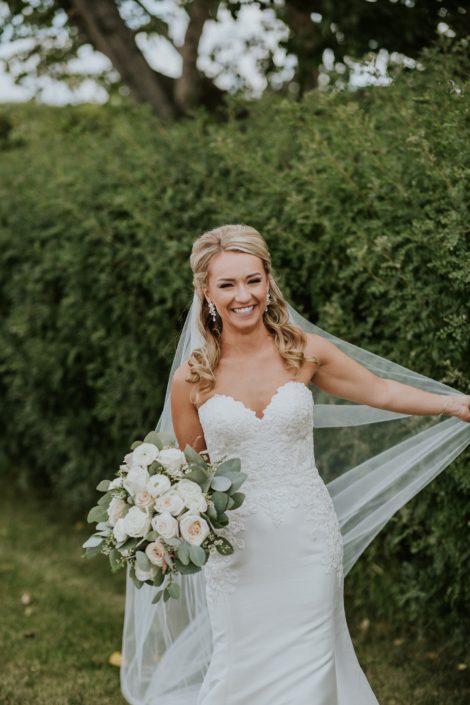 Brooke holding her veil and a blush and ivory bridal bouquet made of white o'hara garden roses, ranunculus, quicksand roses, playa blanca roses, astilbe, wax flower and eucalyptus greenery.
