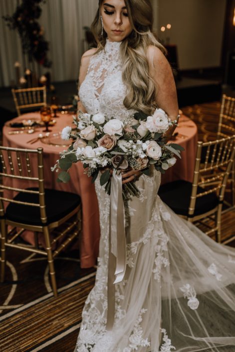 Cambridge Bridal Show 2020 - model wearing lace gown and carrying a bridal bouquet of blush and ivory roses with greenery and trailing ribbons.