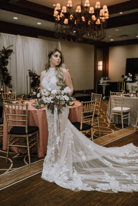 Cambridge Bridal Show 2020 - model wearing lace gown and carrying a bridal bouquet of blush and ivory roses with greenery and trailing ribbons.