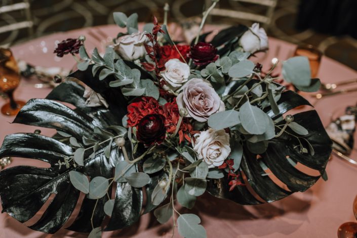 Cambridge Bridal Show 2020 - low centrepiece with black monstera leaves, red roses, blush roses, red ranunculus and eucalyptus greenery.