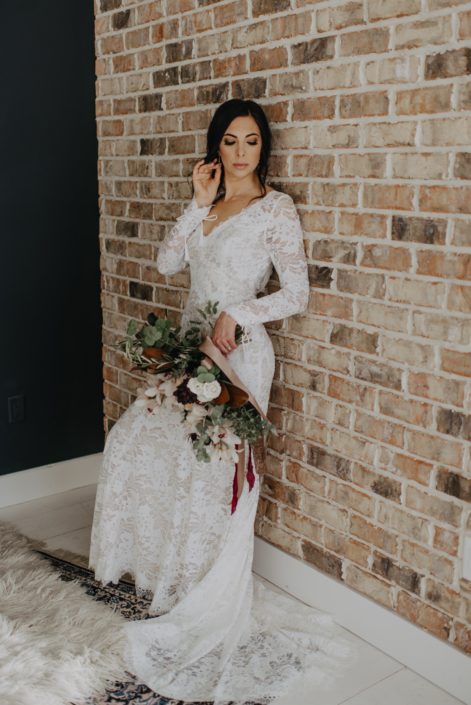 Neutrals Styled Shoot with Down the Aisle - Bride wearing lace gown holding a neutral coloured bouquet with ivory flowers and greenery tied with trailing ribbons.