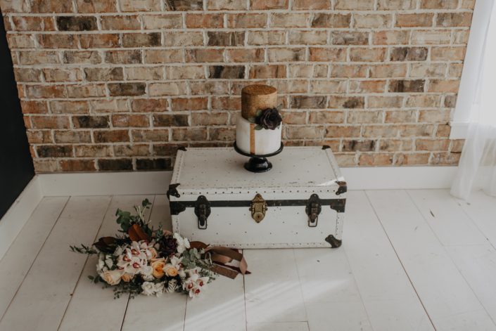 Neutrals Styled Shoot with Down the Aisle - Neutral coloured bouquet of orchids, roses, magnolia leaves and eucalyptus greenery beside a vintage trunk with a cake on top.