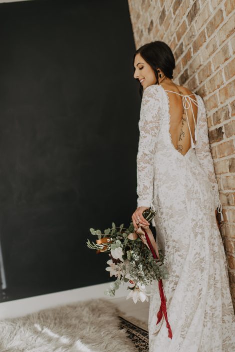 Neutrals Styled Shoot with Down the Aisle -Bride wearing lace gown holding a neutral coloured bouquet with ivory flowers and greenery tied with trailing ribbons.