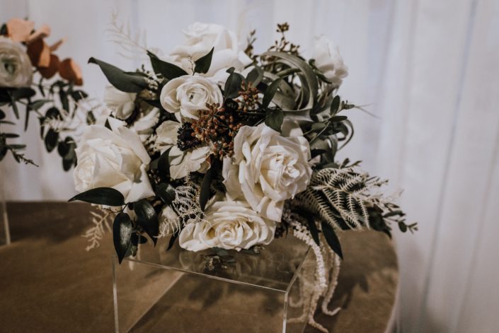 An arrangement designed with an air plant, ivory roses, white hanging amaranthus, and eucalyptus greenery.
