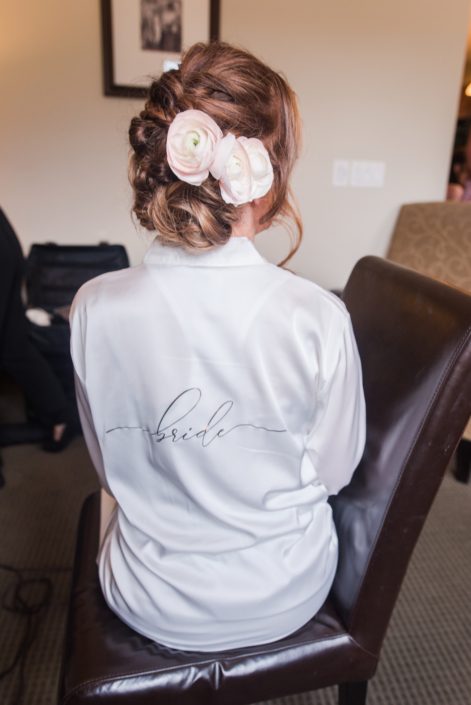 Bride Amy wearing a white bridal robe with blush pink ranunculus hair flowers.