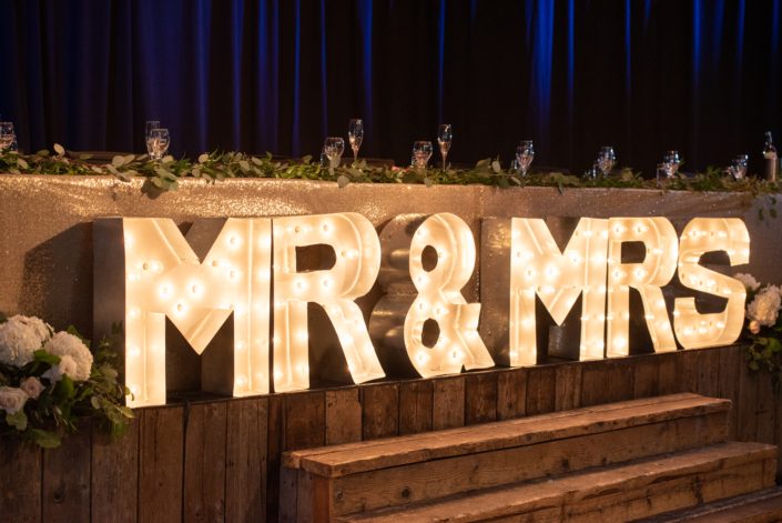 Fresh loose eucalyptus and Italian ruscus greenery atop the head table with a lit up Mr & Mrs sign.