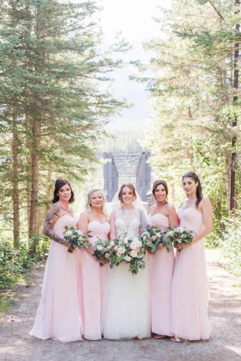 Amy and her bridesmaids carrying pink and blue bouquets featuring white o'hara garden roses, quicksand roses, ranunculus, astilbe, delphinium, eryngium and eucalyptus. The bridesmaids are wearing pink floor length dresses and the bride is wearing a white embroidered bridal gown.