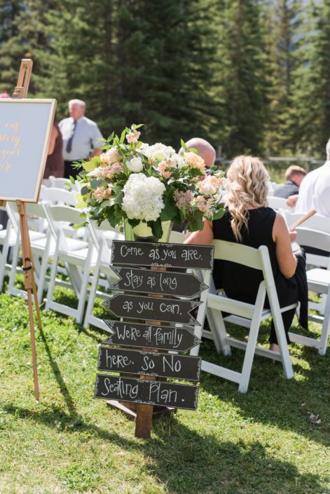 Wedding ceremony sign and urn floral arrangement made of white hydrangea, white o'hara garden roses, quicksand roses, astilbe, peach chrysanthemum, salal and eucalyptus greenery.