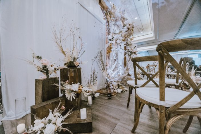 Floral arrangements at the 2020 Down the Aisle Wedding Show designed with dried foraged grasses and branches, pink ranunculus, playa Blanca roses, eucalyptus, and pampas grass on wooden crates.
