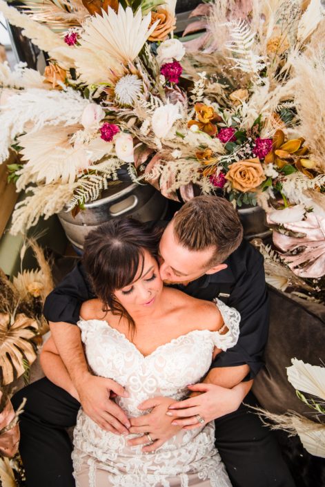 Bride and groom in the truck bed of the Prohibition Pickup surrounded by dried botanicals including palm, pampas grass, metallic painted monstera leaves, roses and ranunculus.