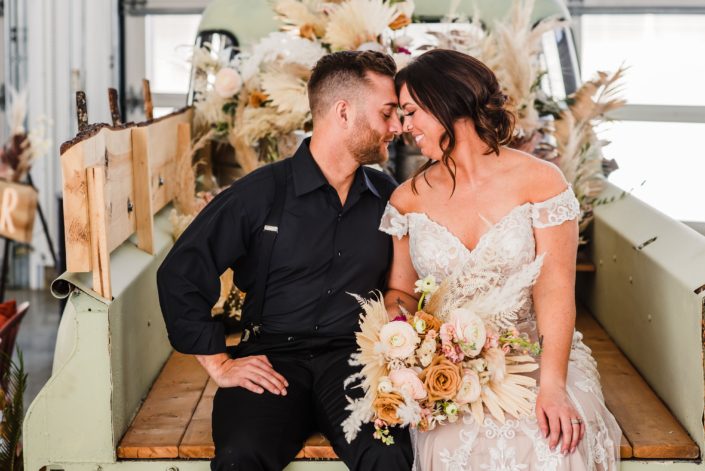 Bride and groom sitting on the tailgate of the Prohibition Pickup. Bride is holding a boho bouquet made of dried palm, pampas grass, roses and ranunculus.