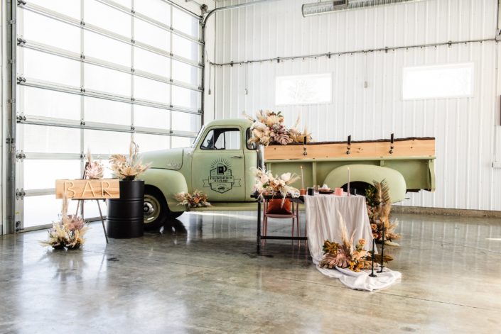 The Prohibition Pickup surrounded by dried floral arrangements, a black barrel, a bar sign and a sweetheart table.