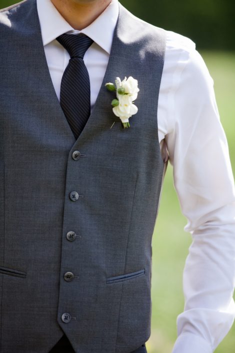 Groom wearing a grey vest with a ivory spray rose boutonniere accented with greenery.