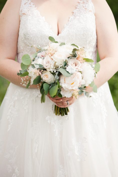 Bride wearing ivory lace bridal gown and holding cream and blush bouquet featuring white peonies, white o'hara garden roses, quicksand roses, babies breath, pale pink astilbe, dusty miller and a mixed variety of eucalyptus.
