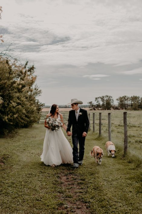 Erika and Colt's Blush and Mauve Country Wedding - bride and groom are walking hand in hand with two dogs and Erika is holding a blush, white and ivory bridal bouquet.