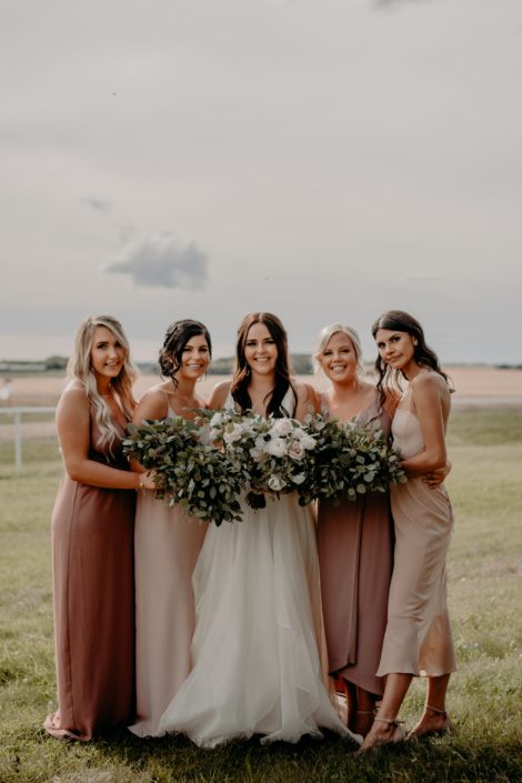 Erika and Colts blush and mauve country wedding - bride wearing white dress and carrying a blush, ivory and white bouquet featuring panda anemones, quicksand roses, ranunculus and lisianthus. The bridesmaids are wearing mauve dresses and carrying fresh mixed eucalyptus bouquets.