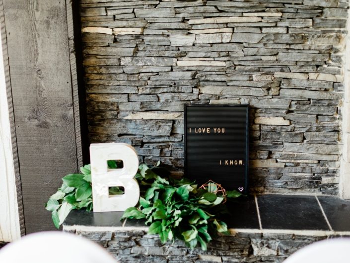 Letter "B", black letter board sign, geometric decor and lush greenery garland on a fireplace hearth.