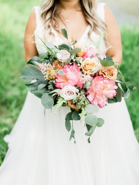 Modern Coral Charm Peony bouquet accented with golden mustard roses, quicksand roses, cappuccino roses, astilbe, astrantia, monstera leaf, boston fern and eucalyptus greenery.