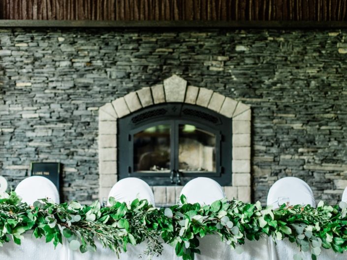 Head table in front of grand fireplace at Canyon Ski Resort with fresh greenery garland made of salal and eucalyptus.