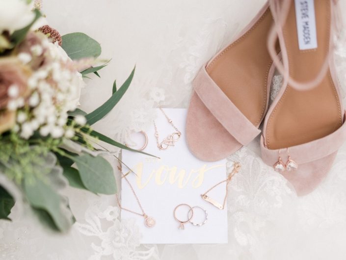 Bride's dusty rose shoes with bouquet, veil, vows and rose gold jewelry flat lay.