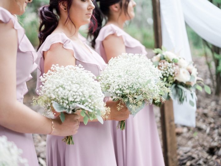 Bridesmaids wearing dusty rose gowns and holding gyposphelia (babies breath) bouquets.