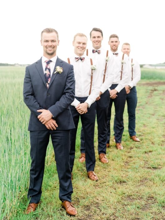 Groom wearing rose gold boutonniere with groomsmen wearing suspenders and babies breath boutonnieres.
