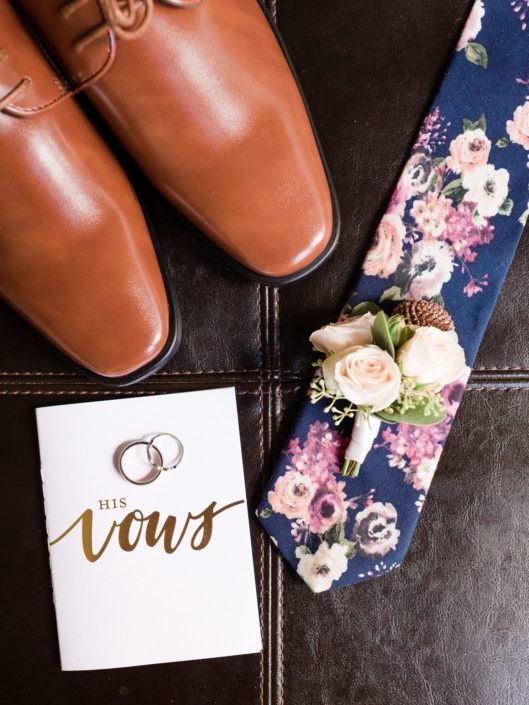 Groom's tie, shoes, boutonniere, vows and rings flat lay.