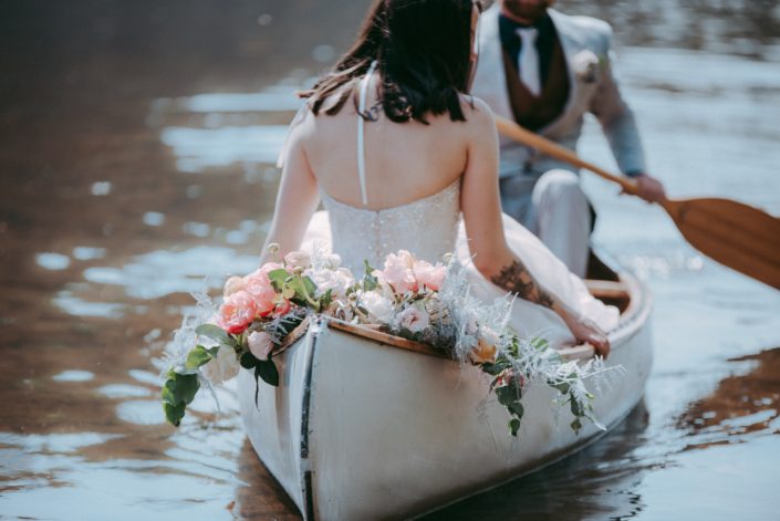 Canoe adorned with blush and coral bouquet featuring quicksand and playa blanca roses, coral charm peonies, peach ranunculus, pale pink astilbe, silver plumosa and a mixed variety of eucalyptus greenery.