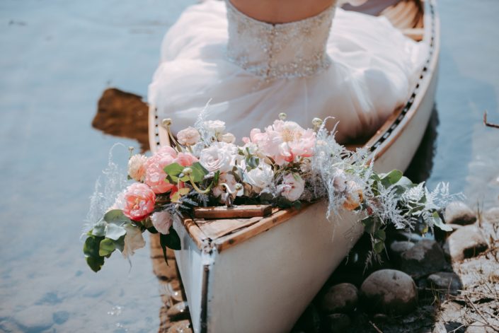 Canoe and a bridal bouquet featuring coral charm peonies, blush roses, silver plumosa and eucalyptus greenery.