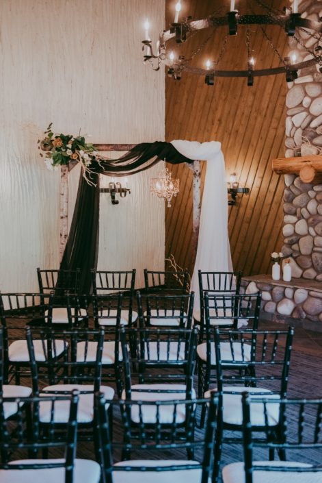 Black and white chiffon draped on a birch archway adorned with a corner floral arrangement of mazanita branches, tulips, quicksand roses and toffee roses.