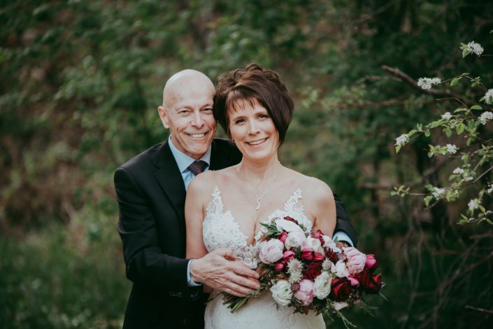 Sandra and David embracing with an elegant pink and burgundy bridal bouquet designed with peonies, ranunculus, black bacarra roses, scabiosa, tulips, Helleborus, Astrantia and, maple leaves, juniper, purple sage and Eucalyptus greenery.