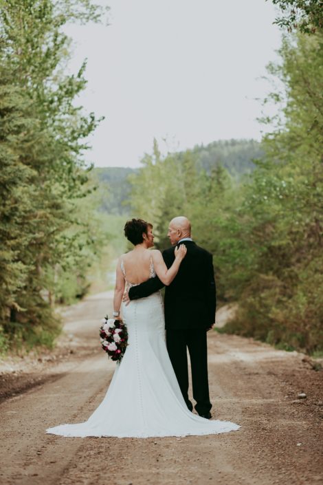 Bride and groom walking with arms around each other while bride holds an elegant pink and burgundy bouquet featuring helleborus, Sarah Bernhardt peonies, ranunculus, Black Bacarra Roses, Blackberry Scoop plum scabiosa, tulips, astrantia and eucalyptus.
