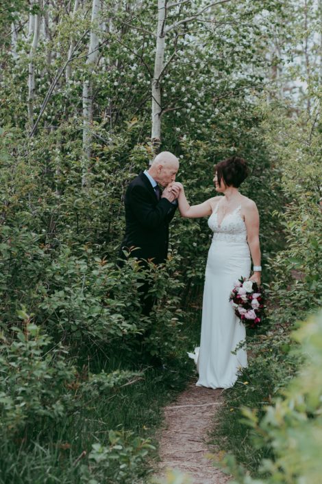 Groom kissing bride's hand while she is holding a pink and burgundy bridal bouquet made with helleborus, peonies, ranunculus, black bacarra roses, plum scabiosa, tulips, astrantia and eucalyptus.