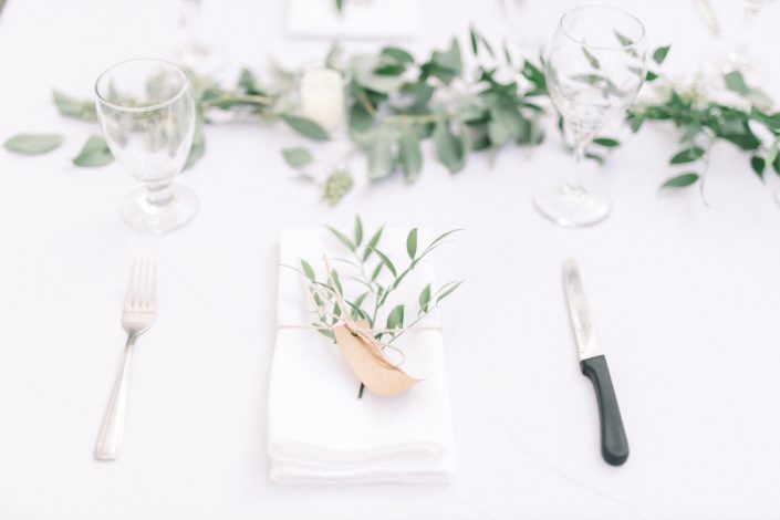 Timeless white wedding place setting, folded linen napkin with fresh italian ruscus, twine and name tag.