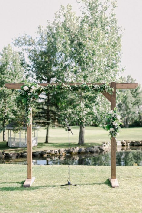 Simple outdoor ceremony archway covered with fresh greenery and white flowers.
