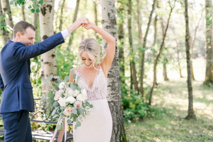 Kayla and Joel dancing while Kayla holds a bridal bouquet designed with white o'hara garden roses, white ranunculus, quicksand roses, white astilbe, olive branches and fresh eucalyptus.