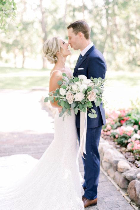 Bride and groom with a timeless white wedding bridal bouquet designed with white o'hara garden roses, quicksand roses, white ranunculus, white astilbe, olive branches and fresh eucalyptus greenery.