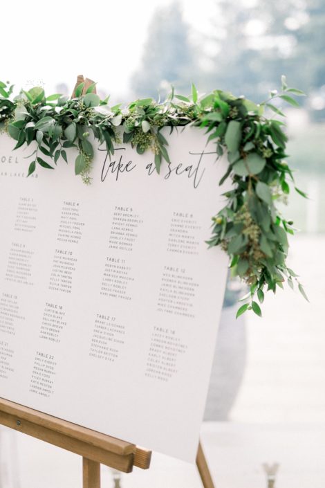 Fresh greenery garland on the seating chart for Kayla and Joel's Timeless White Wedding.