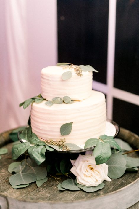 Simple white tiered cake decorated with eucalyptus greenery and a white Tibet rose.