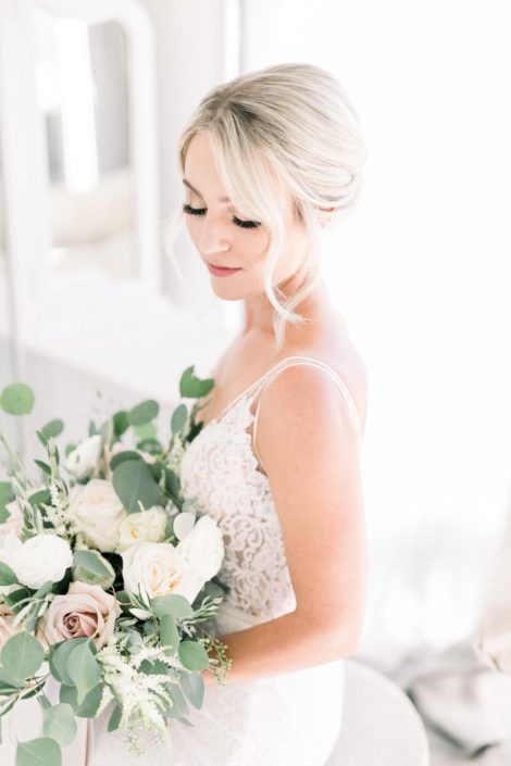Close-up of Kayla holding her bridal bouquet designed with white o'hara garden roses, white ranunculus, quicksand roses, white astilbe, olive branches and fresh eucalyptus.