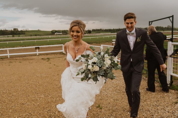 Bride and groom with a white and grey green bridal bouquet made of Playa Blanca roses, lisianthus, astilbe, blue star succulents, dusty miller and a variety of eucalyptus greenery.