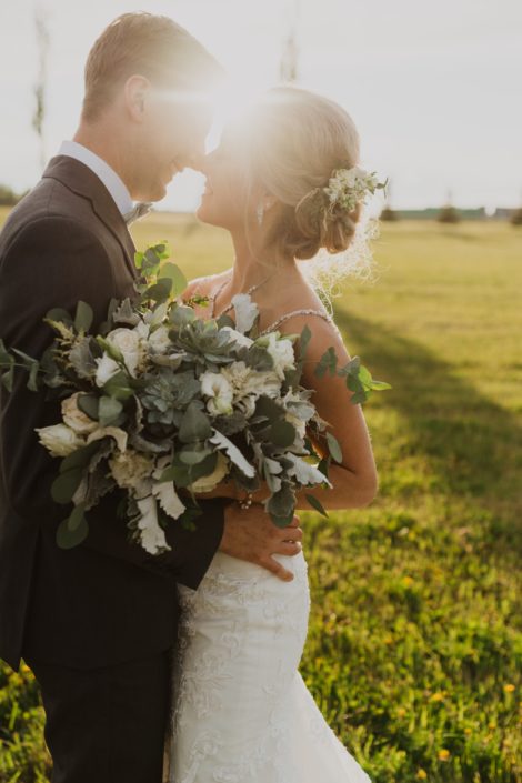 Bride and groom in the sunshine; bride hair flowers designed with white spray roses, astilbe, lisianthus and grey toned greenery; bridal bouquet featuring white Playa Blanca roses, white lisianthus, white astilbe, Blue Star succulents, dusty miller and eucalyptus.