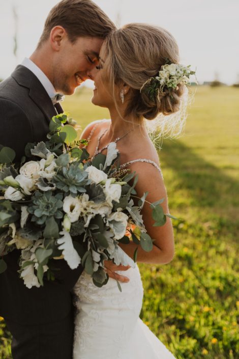 Leah and Chance; bride hair flowers made of white spray roses, lisianthus and astilbe with a touch of grey toned greenery; bridal bouquet with a vintage feel designed with white playa blanca roses, lisianthus, astilbe, Blue Star succulents, dusty miller and eucalyptus.