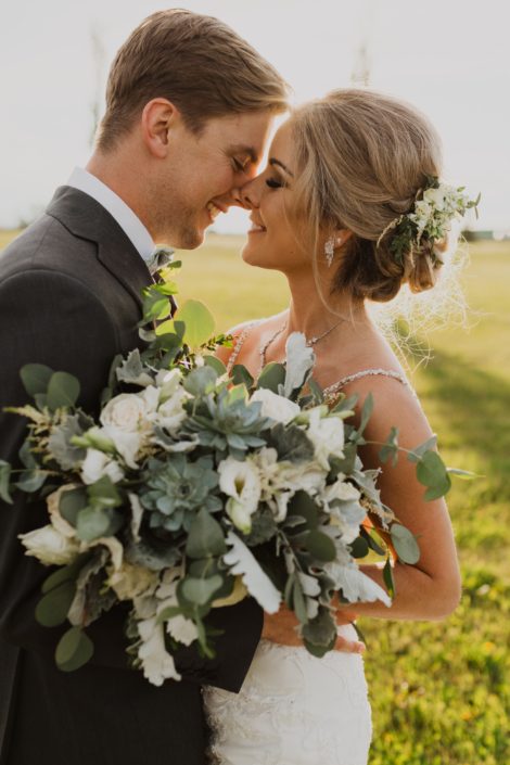 Leah and Chance; white and grey green bridal bouquet with a vintage feel designed with Playa Blanca roses, lisianthus, astilbe, dusty miller, blue star succulents, and a mixed variety of eucalyptus greenery; bride hair flowers.