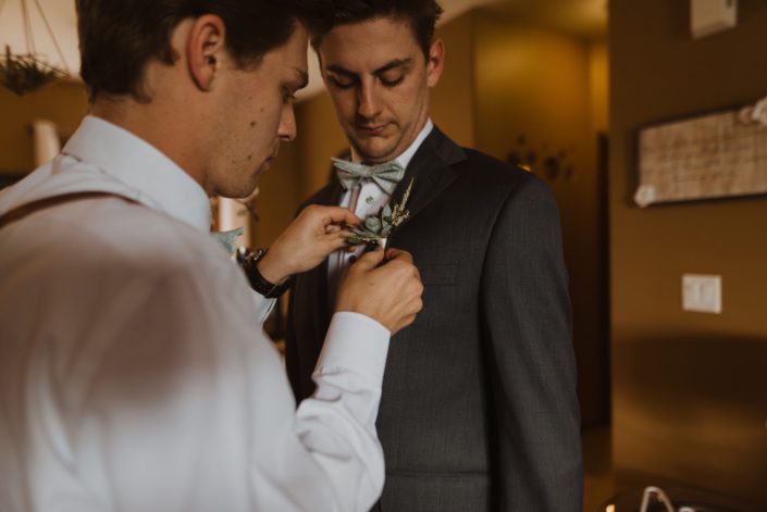 Groom getting his boutonniere pinned on; it was designed with a single small succulent accented by white astilbe and a touch of greenery.